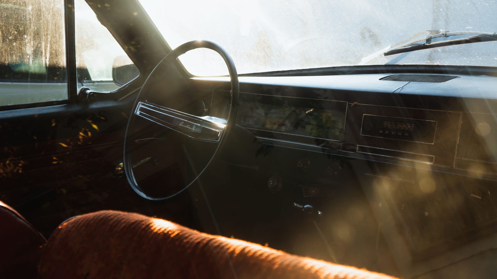 Sunlit interior of a vintage car highlighting the dashboard and steering wheel with a retro feel.