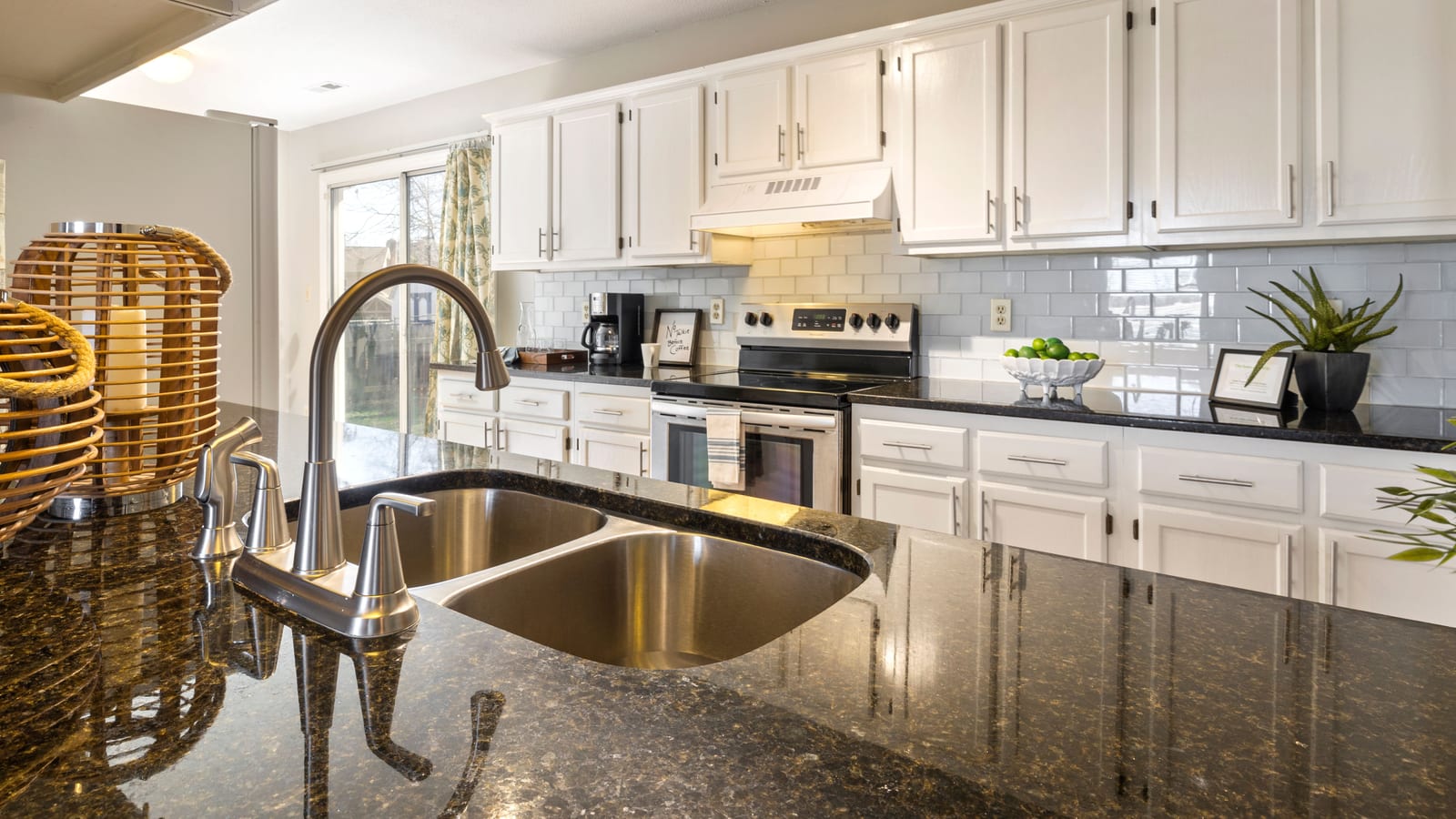 A stylish, contemporary kitchen featuring granite countertops, stainless steel sink, and white cabinets.